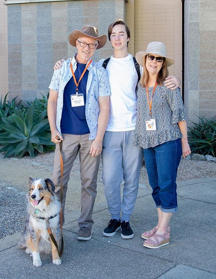 a mother and father pose with their student and the family dog